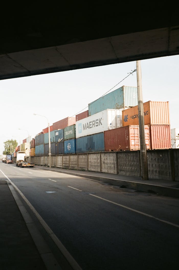 Multicolored cargo containers stacked beside a busy urban street under a clear sky.